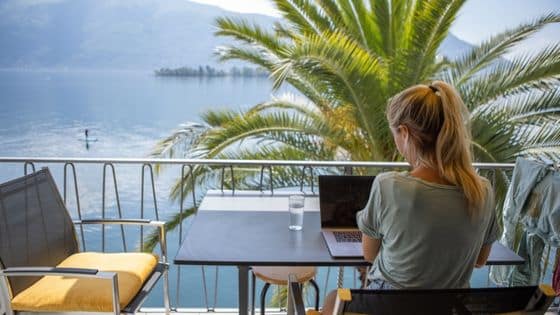bookingsync - une femme travaillant sur son PC sur son balcon devant la mer et un palmier