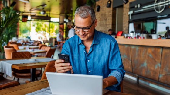 logiciel gestion franchise - un homme assis à une table de restaurant devant son PC consultant son téléphone portable