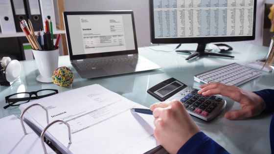 logiciel de facture avec retenue de garantie - quelqu'un en train de faire sa facturation sur un bureau avec une calculatrice, un pc et un classeur avec des factures