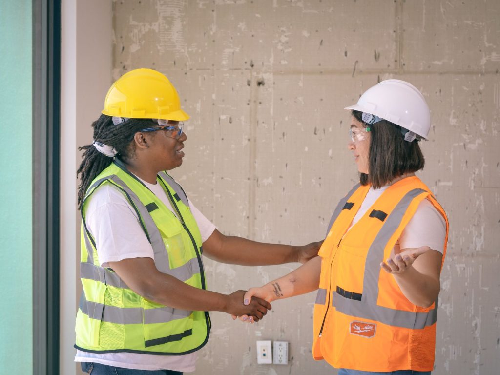 Deux professionnels du bâtiment en équipement de sécurité se serrant la main sur un chantier, symbolisant le rachat d’une entreprise de travaux