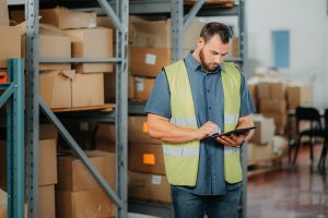 Gestion des stocks d'un entrepôt, tablette et homme travaillant dans un bâtiment de stockage pour superviser la livraison.
