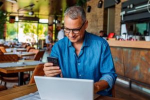 logiciel gestion franchise - un homme assis à une table de restaurant devant son PC consultant son téléphone portable