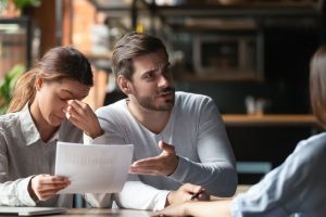 Angry young couple complaining, bad contract terms, outraged man arguing with manager or Real Estate Agent, upset woman holding documents with stats, contract, dissatisfied clients demanding compensation